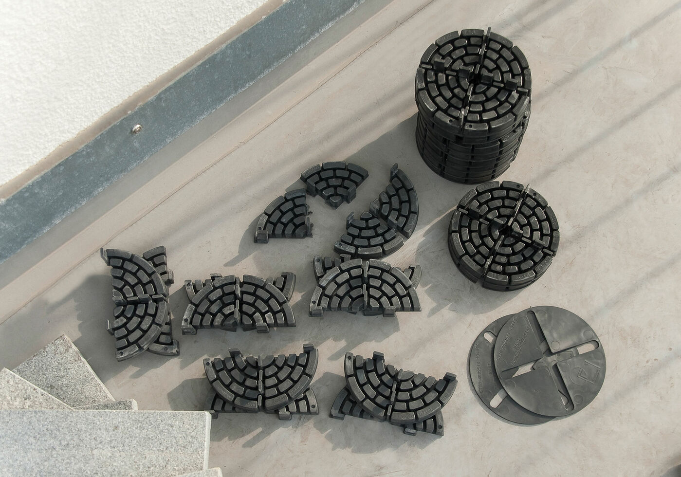 Black segmented circular plastic floor leveling supports arranged on a light concrete surface near stairs.